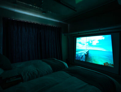 Cozy bedroom with a projector screen displaying scenic views at Bayside Villa Miyakojima.