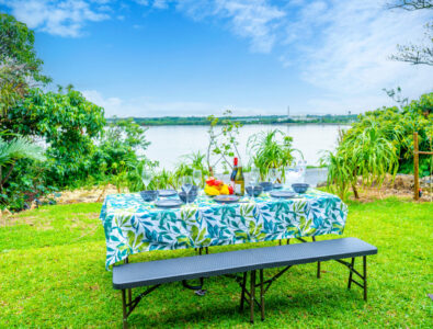 Outdoor picnic table set with wine, fruits, and tableware, overlooking a lush garden and ocean at Bayside Villa Miyako Iland.