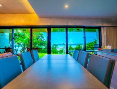 Dining area with modern chairs and large windows offering a lush garden and ocean view at Bayside Villa Miyako Iland.