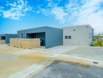 Modern exterior of Bayside Villa Miyako Iland with stone walls and concrete driveway under a clear blue sky.