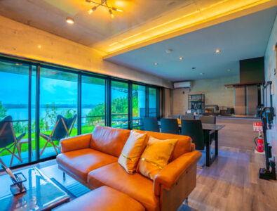 Spacious living and dining area with a leather sofa and large windows overlooking the ocean at Bayside Villa Miyako Iland.
