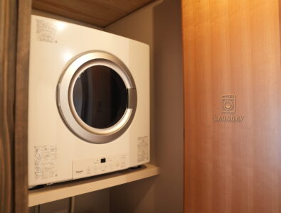 Compact laundry area with modern dryer and wooden door at Enishiya Izumo.