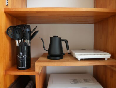Wooden kitchen shelf with electric kettle, induction cooktop, and kitchen utensils at Ocean Villa Tokunoshima.