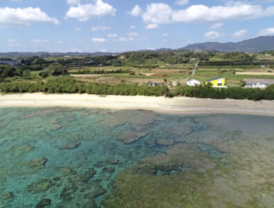 Aerial view of Ocean Villa Tokunoshima with beach and crystal-clear water in the foreground.