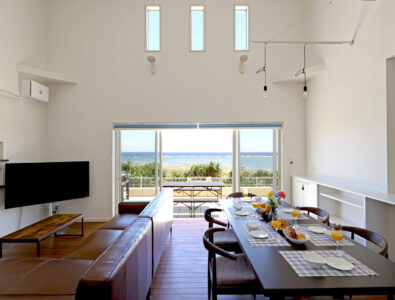Spacious living and dining area with a large window offering an ocean view at Ocean Villa Tokunoshima.