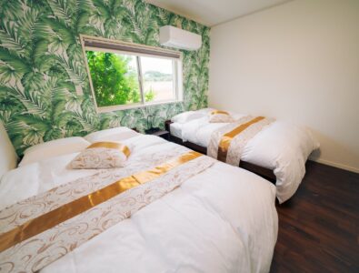 Tropical-themed bedroom with double beds and palm leaf wallpaper at Ocean Villa Tokunoshima.